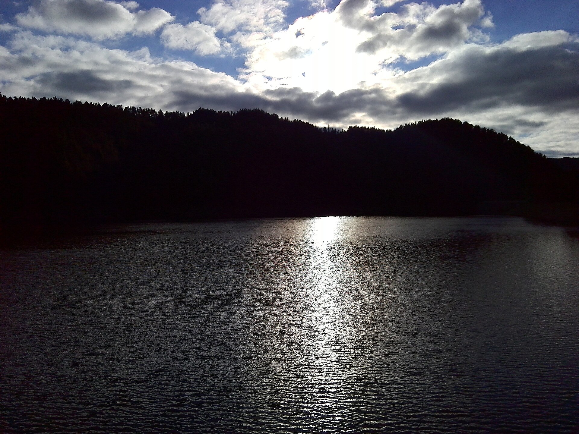 Sunlight reflected on Berovo Lake beneath a cloudy sky.