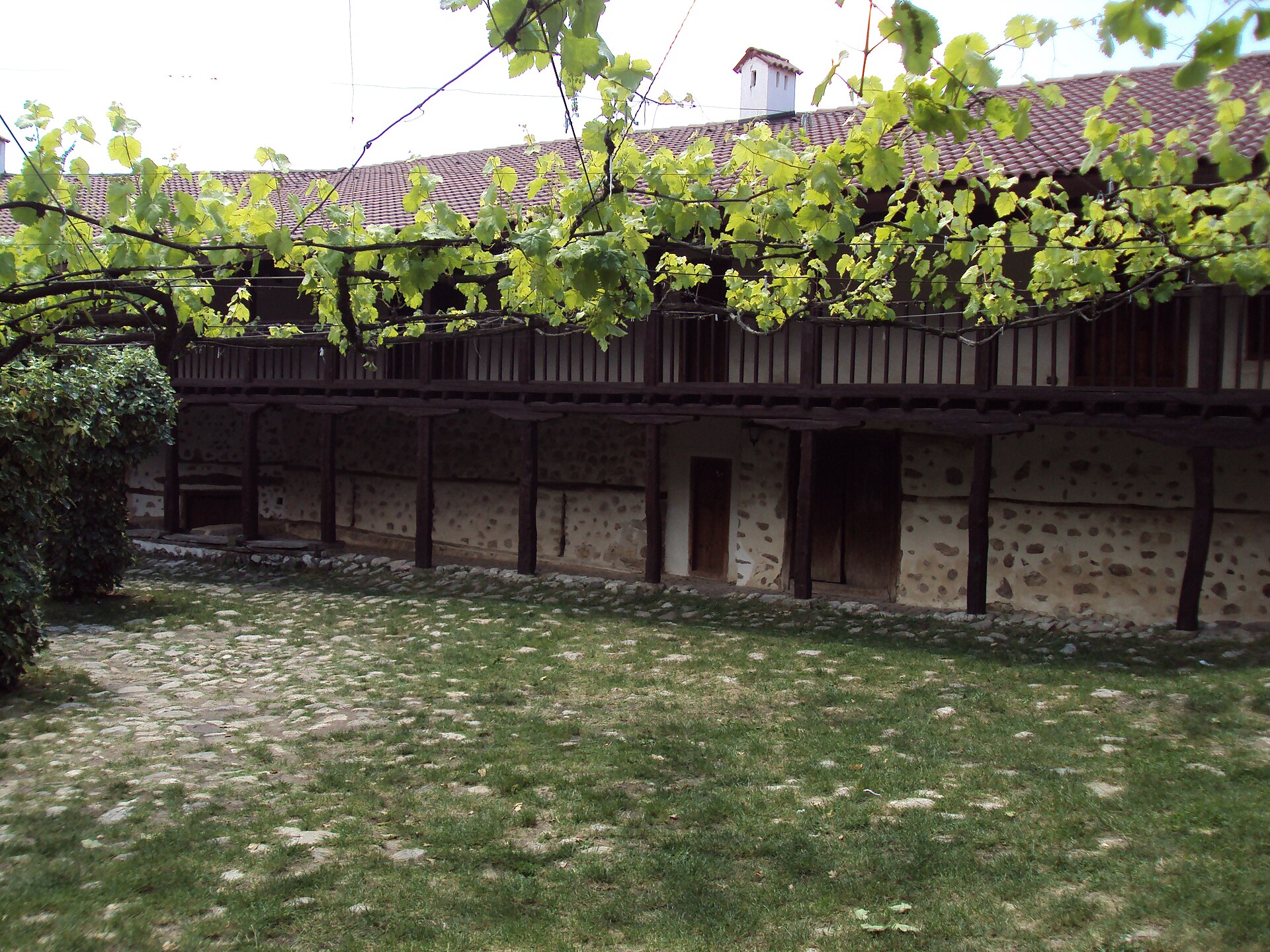 A vine-covered wooden gallery overlooking the courtyard at Rozhen Monastery.